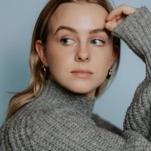 Zacht en natuurlijk portret van een jonge vrouw met blond haar en blauwgrijze achtergrond, gefotografeerd door Studio SamSam